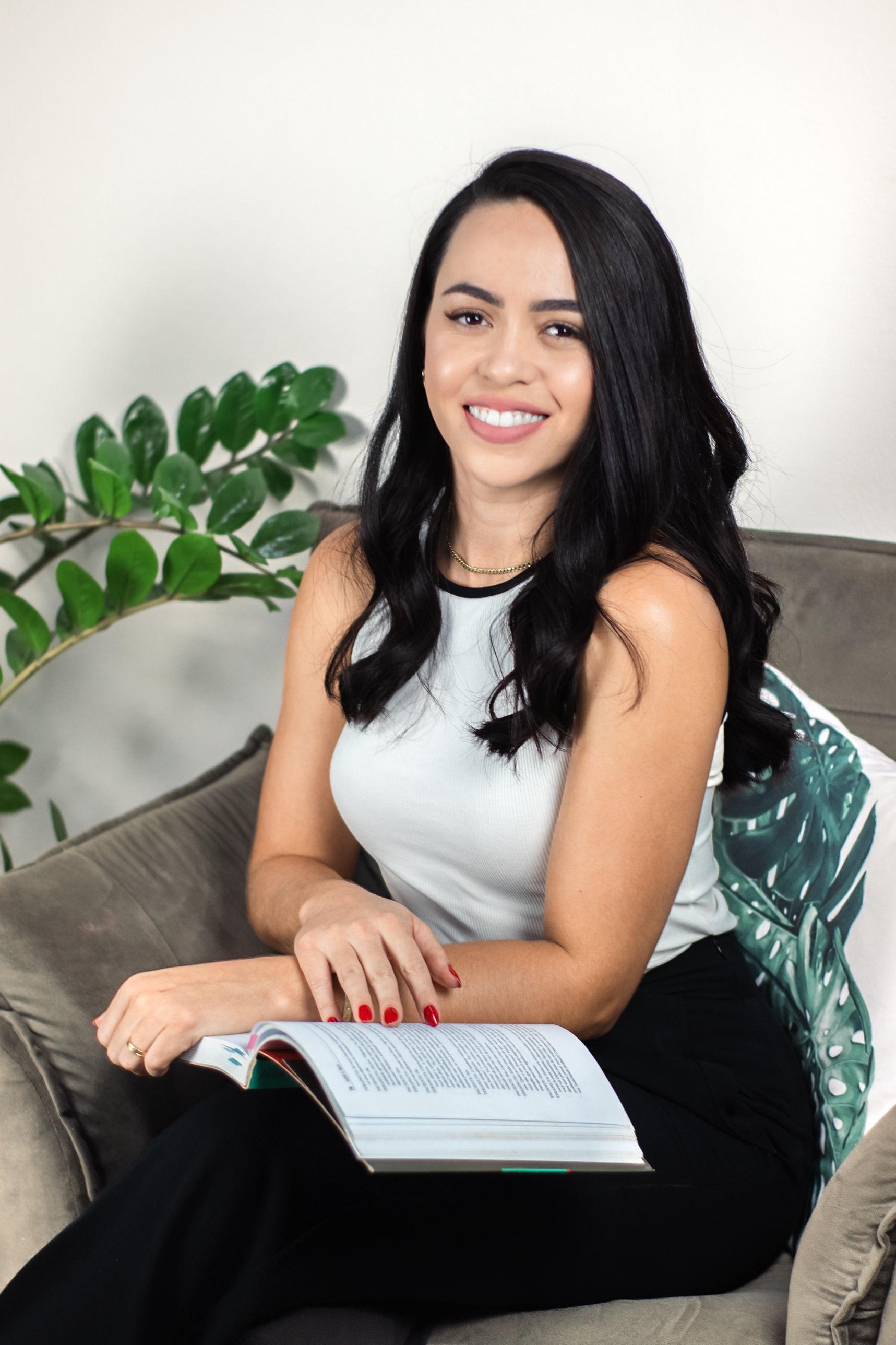 Psicóloga Rosana Ruiz sorrindo, sentada em um sofá com um livro aberto